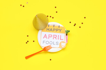 Table setting with festive postcard and party decor for April Fools Day on yellow background