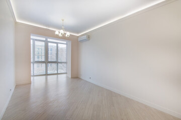 An empty bright room without furniture with a high ceiling, laminate flooring and access .to the loggia.