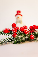 Festive New Year's decoration, decor from a Christmas tree branch and red berries on a background of a ceramic snowman with a red hat and a bow.