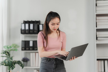 Focused and Determined: A young woman, radiating confidence, stands in her office, engrossed in...