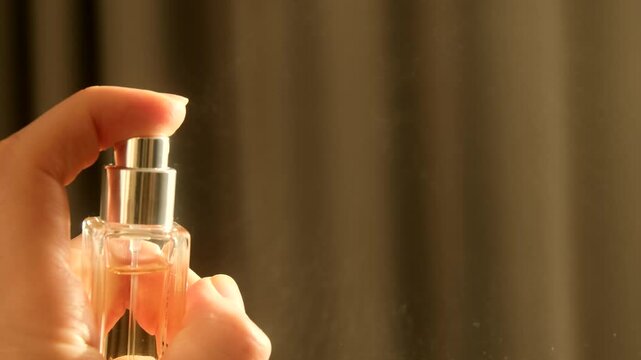Hand spraying dust perfume bottle, releasing a fine mist into the air. Slow motion. Applies perfume. Spraying fragrance with scent.