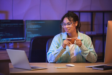 Fototapeta premium Young African-American QA engineer drinking coffee in office at night