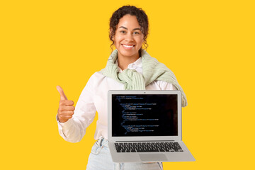 Young African-American QA engineer holding laptop with programming code and showing thumb-up on...