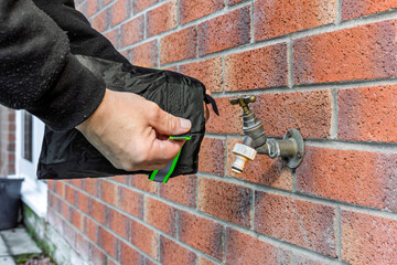 Person Installing Winter Frost Protection Insulated Tap Cover on Brass Garden Brick Wall Water Faucet