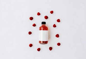 Glass bottle with black caps, filled red kombucha and raspberries ingredients on a white background