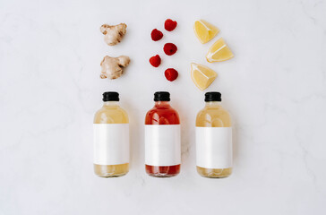 Three small transparent glass bottles with black caps, filled with colorful kombucha of yellow, red, and green and ingredients