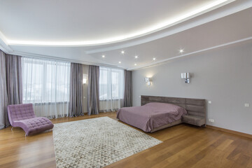 A luxurious bedroom with light walls and parquet. A wide bed and an original lilac armchair.