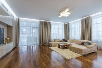 Luxurious living room with panoramic windows, parquet. Built-in wardrobe and beige sofa on a soft carpet.