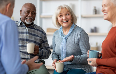 Multiracial group of positive senior men and women sitting in circle, drinking tea and having conversation, smiling and laughing, having home party or enjoying time at nursing home, closeup - Powered by Adobe