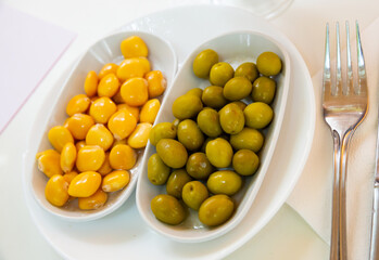 Two white plates with delicious green unpitted olives and pickled lupin beans