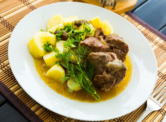 Stewed tasty lamb with mushrooms and potatoes served at plate with greens