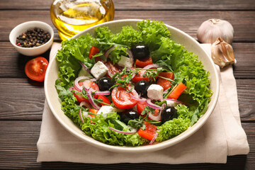 Bowl of tasty Greek salad and ingredients on wooden table