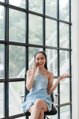 Happy Businesswoman on Phone Call: A young woman in a blue dress smiles while talking on her phone, radiating confidence and success, a captivating image for business and technology concepts.