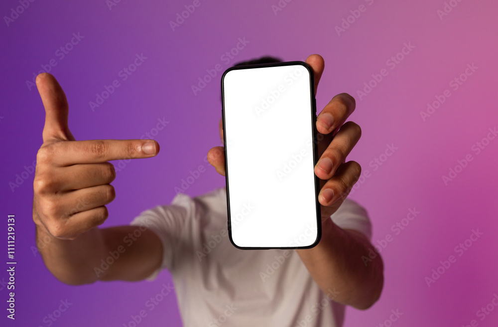 Poster unrecognizable young man holding smartphone in front of his face, pointing at empty screen, offering