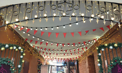 Obraz premium Garlands of light bulbs and red flags hang in the arch between the houses.