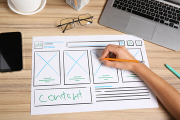 Developing UI design. Designer with smartphone creating website wireframe on paper at wooden table,...