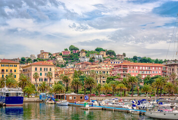 Fototapeta premium La Spezia, Italy - May 27 2018: View of the port seen from the sea, with lot of boats, palm trees and seaside houses on the background.
