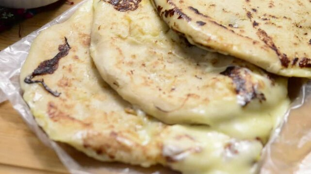 A smooth video pan showcasing cheese-filled pupusas with curtido and sauce on a wooden surface, highlighting Salvadoran culinary tradition.