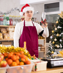 Young guy seller raises glass of champagne in grocery store decorated for christmas