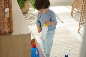 Little boy playing with bottles of detergents near cabinet at home. Child in danger