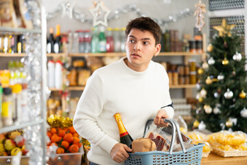 Man with a grocery basket full of food for the holiday in a Christmas supermarket. Guy next to the counter chooses food for the New Year