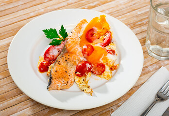 Dish of tasty scrambled eggs with salmon and tomatoes at plate on table