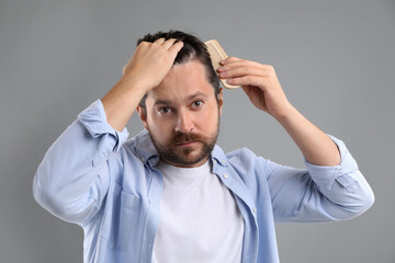 Man brushing his hair on gray background. Alopecia problem