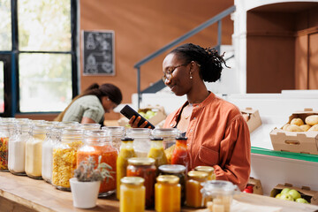 Young black woman using smartphone while browsing through the eco friendly store. African american...