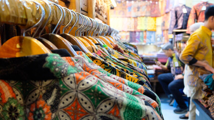 A close-up shot of colorful batik shirts hanging on wooden hangers in a market stall, with a selective focus on the front row