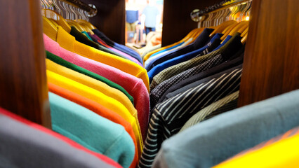 A colorful display of clothing items hanging on wooden hangers in a clothing store. The shirts are arranged in rows, with each row featuring a different color