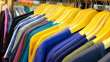 A colorful display of t-shirts hanging on wooden hangers in a clothing store. The shirts are arranged in rows, with each row featuring a different color