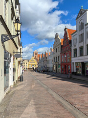A picturesque view of Krämerstraße in Wismar, Germany, showcasing historic architecture, cobblestone streets, and vibrant storefronts under a clear sky. Perfect for travel and cultural themes.