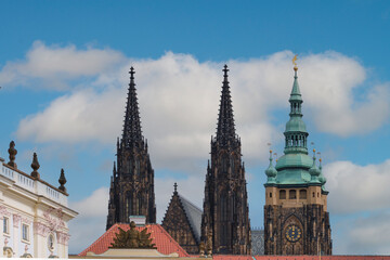 A scenic view of Gothic spires of the famous Hradschin and a Baroque building against a blue sky with scattered clouds, showcasing Prague's historic architecture and cultural heritage.