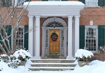 House with portico entrance and colorful Christmas wreath on wood grain front door