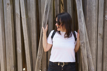 Fototapeta premium Beautiful smiling dark-haired girl in a white T-shirt and with a backpack on her shoulders in the summer on a trip. Pedestrian wanderung concept