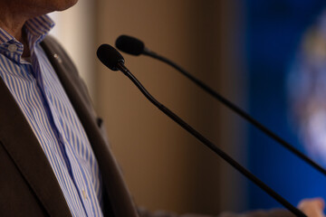 focus sur un micro et les mains d'un orateur prononçant un discours à la tribune lors d'un...