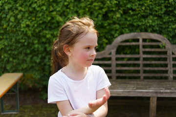 Beautiful cheerful girl in a white T-shirt having fun in the summer outdoors. Concept of an active, mobile, sincere child