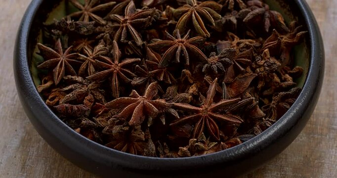 Close-up view of anise stars in bowl on a rustic wooden background. Table spin.