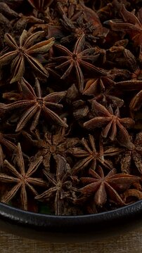 Close-up view of anise stars in bowl on a rustic wooden background. Table spin, vertical video.