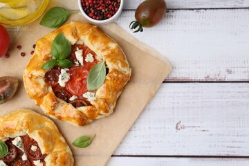 Tasty galettes with tomato, basil and cheese on white wooden table, flat lay. Space for text