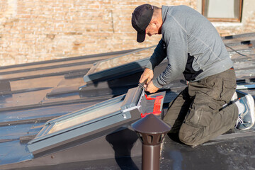 A roofer builder worker finishing folding a metal sheet using special pliers with a large flat grip. A roofer and window master work.