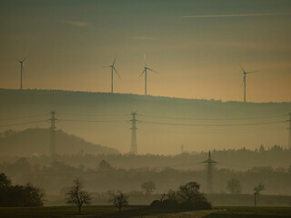 Strommasten und Windräder im Nebel in der Ferne