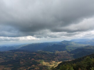 A scenic view of Phu Ruea National Park, Thailand, showcases expansive valleys, lush greenery, and dramatic overcast clouds.