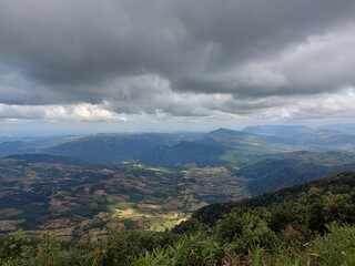 A scenic view of Phu Ruea National Park, Thailand, showcases expansive valleys, lush greenery, and dramatic overcast clouds.