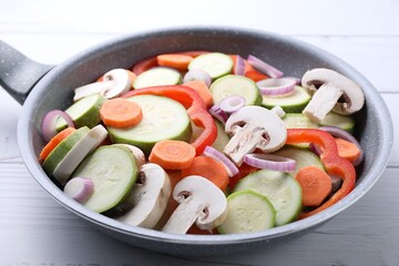 Frying pan with mix of fresh vegetables and mushrooms on white wooden table, closeup