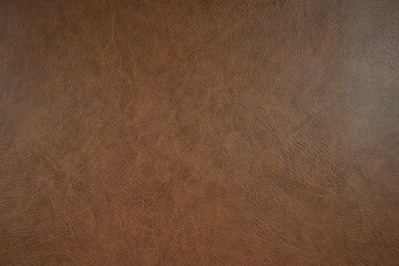 Close-up view of a textured brown leather surface. The texture is detailed, with fine lines and variations in color, ranging from darker to lighter shades of brown.