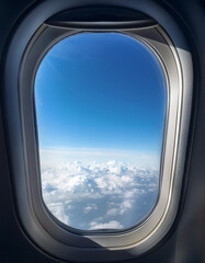 Airplane window with view of blue sky and clouds from inside the plane