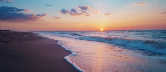 Obraz premium Tranquil ocean waves lapping the sandy shore at sunset.
