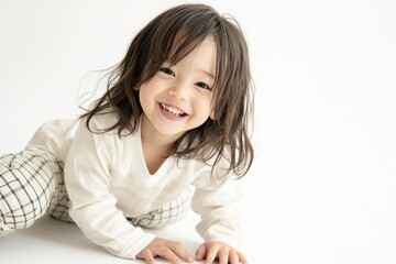 Naklejka premium Photo of a happy, smiling Asian toddler girl wearing a white shirt and plaid pants, sitting on the floor and isolated against a white background. The image was taken in a studio with soft lighting. 