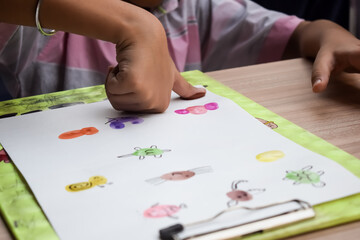 Smart Indian little boy perform thumb painting with different colourful water colour kit during the summer vacations, Cute Indian Kid doing colourful thumb painting drawing on wooden table